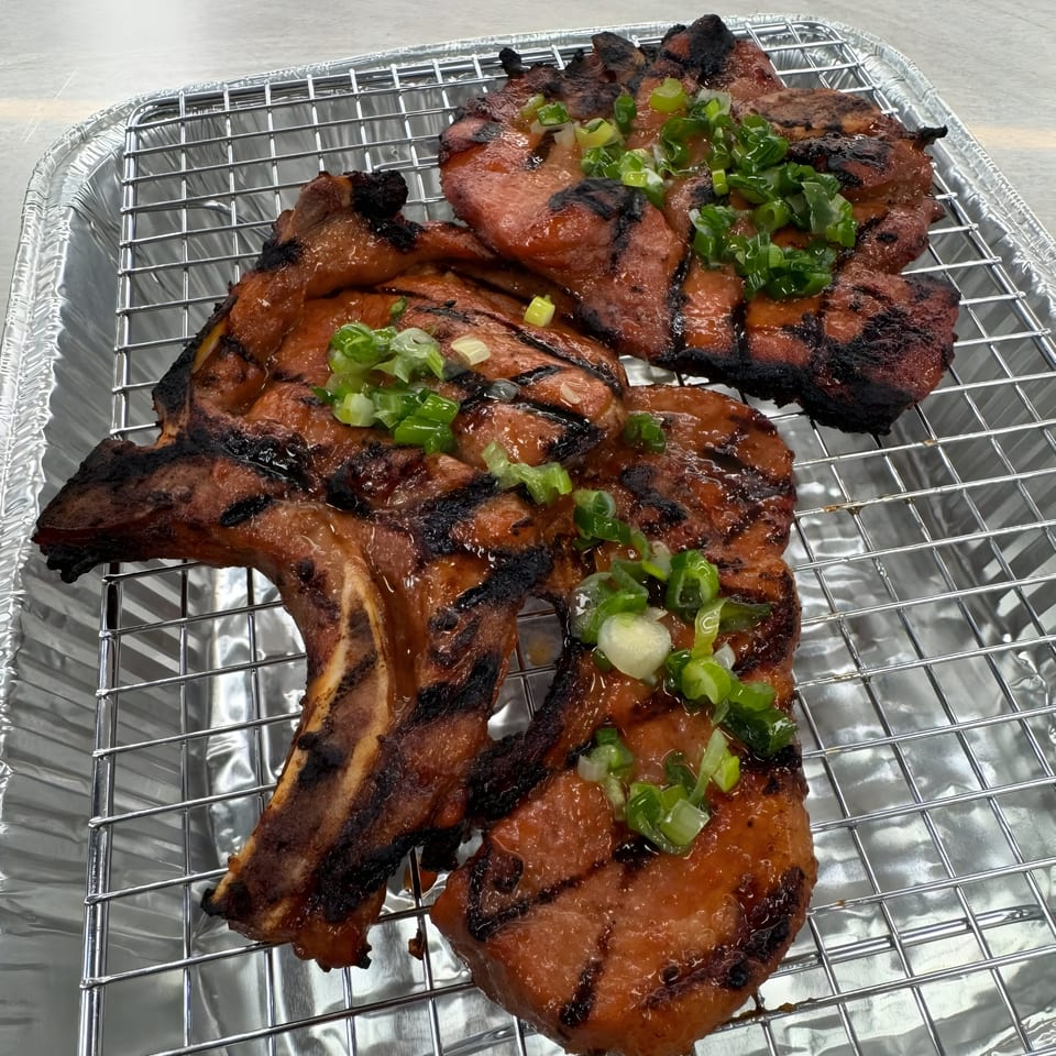 Grilled Vietnamese pork chops, glazed and topped with chopped green onions, in a foil pan.