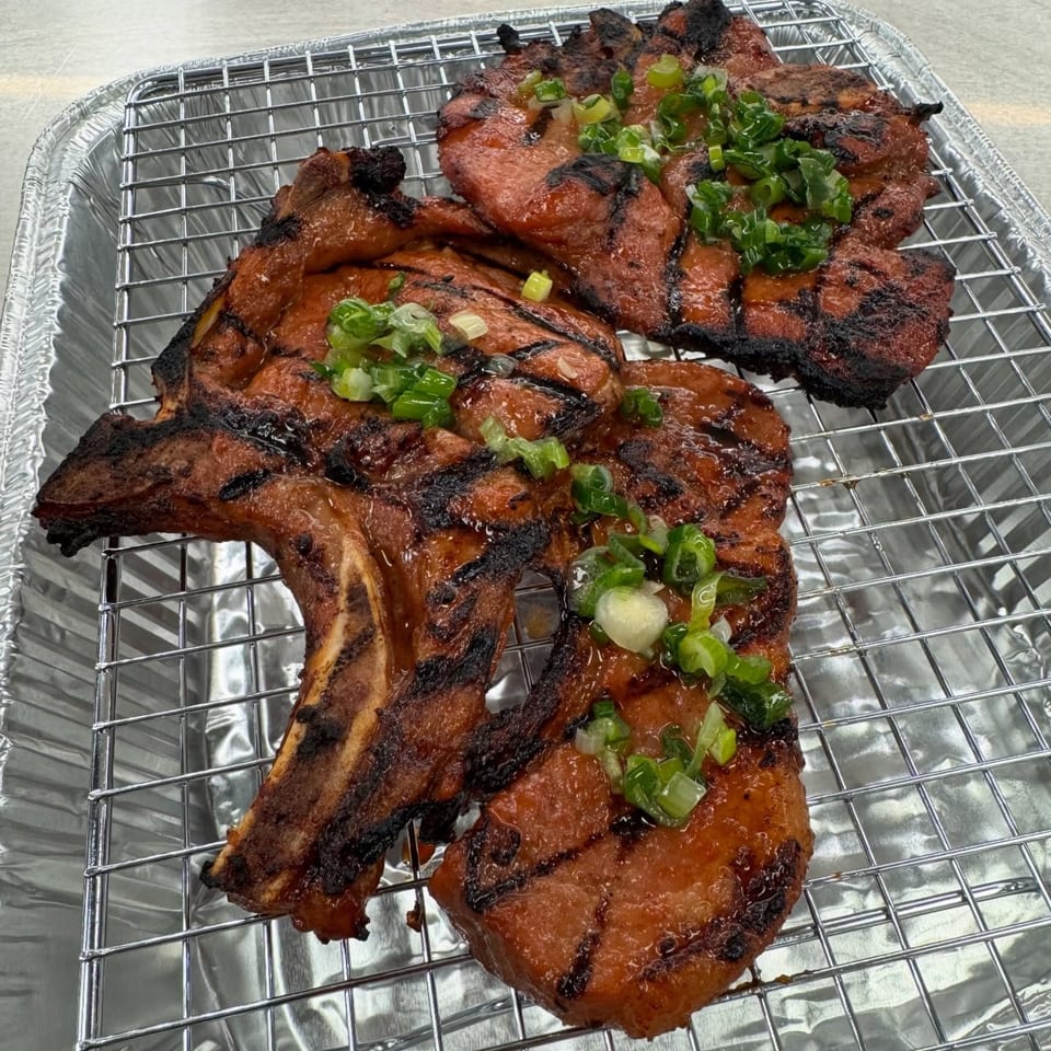 Grilled Vietnamese pork chops with char marks and green onions on a metal rack in a foil pan.