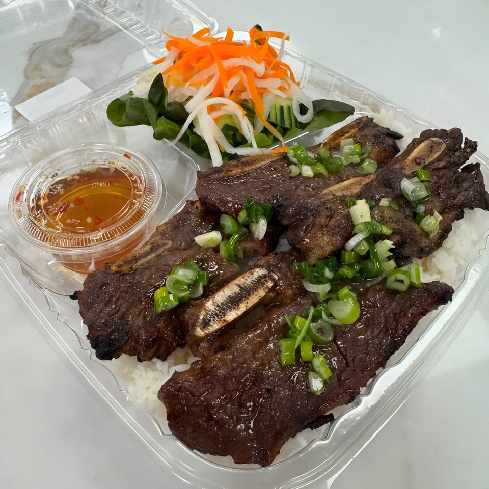 Mama Ha's Eatery's grilled short ribs with rice, pickled vegetables, and dipping sauce in a plastic container.
