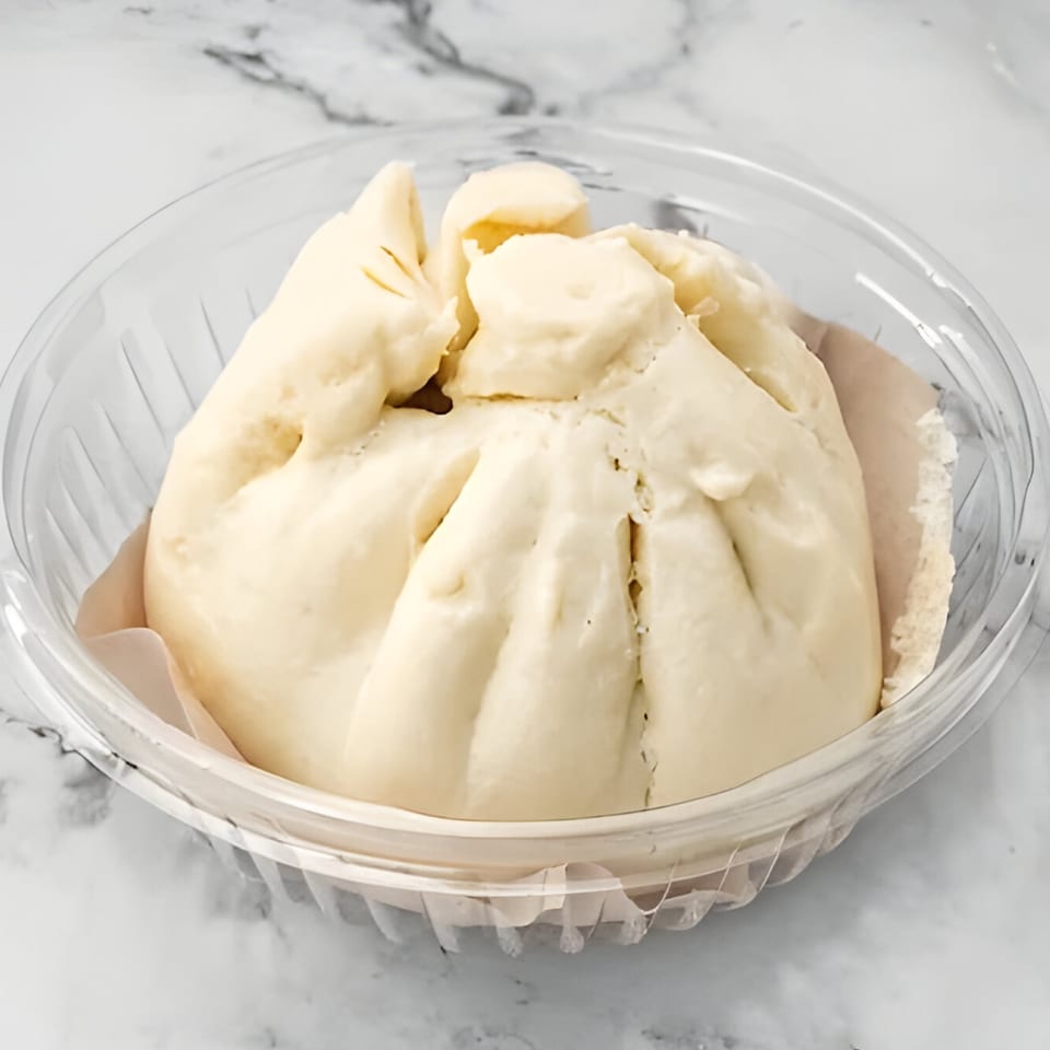 A large, fluffy Vietnamese steamed bun (Banh Bao) in a clear plastic container.